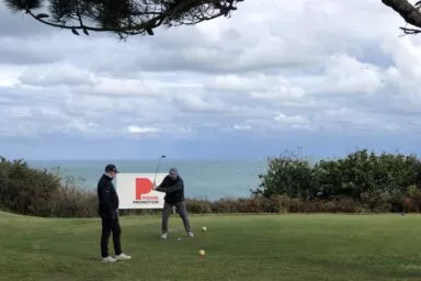 Deux golfeurs en train de jouer au golf pendant le Trophée de Golf Pierre Promotion organisé au Golf Bluegreen de Pléneuf-Val-André, avec à l'horizon la mer.