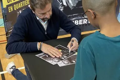 Un tennisman en train de signer un autographe à un enfant pendant l'open en quartier organisé par Pierre Promotion et Rivacom.